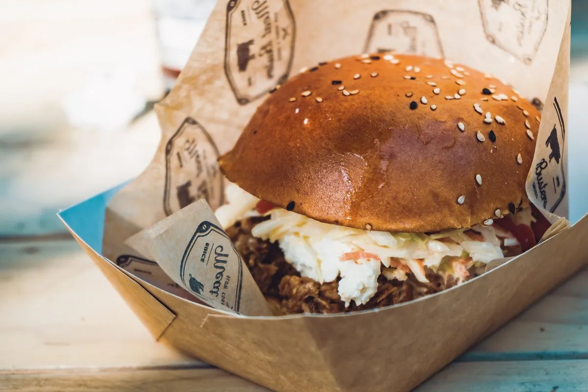 A gourmet burger with fresh toppings in a takeout box, showcasing unique flavors from local restaurants.